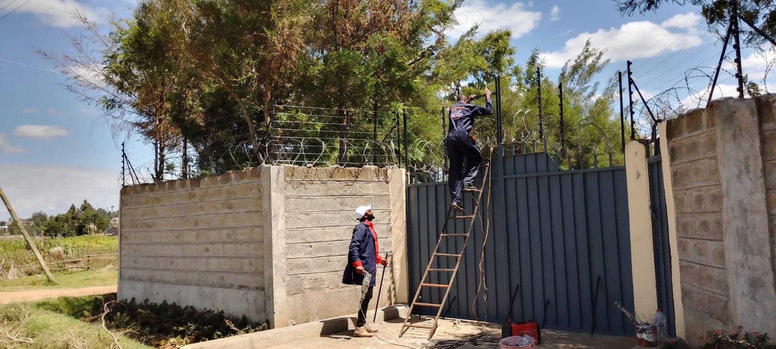 Elatec technicians on a ladder installing electric fence wiring at a Kenyan property